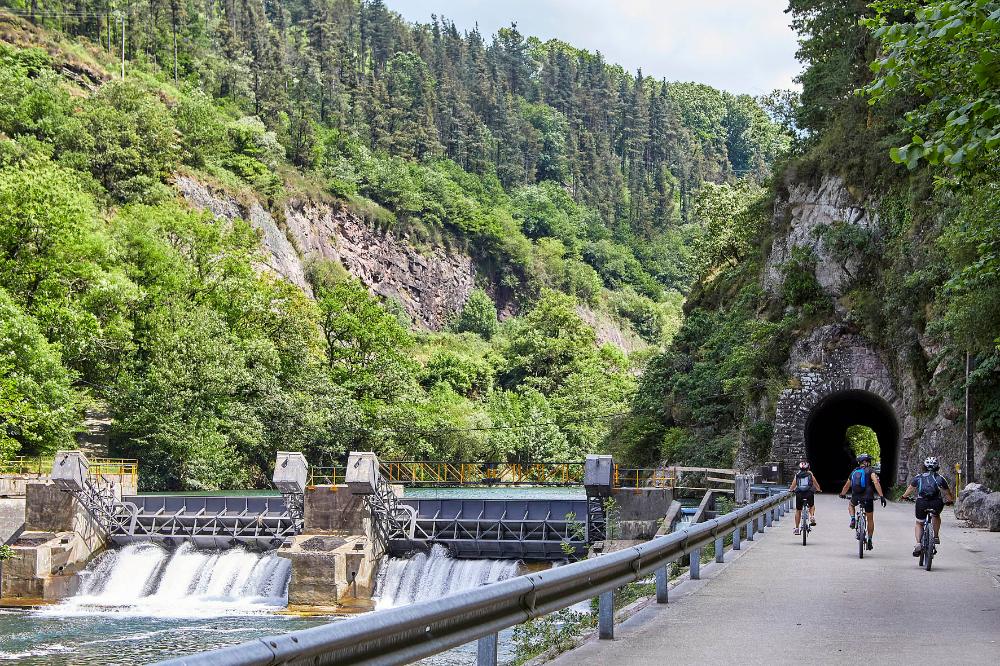 tres ciclistas por la vía verde del Bidasoa al lado de una presa en el río